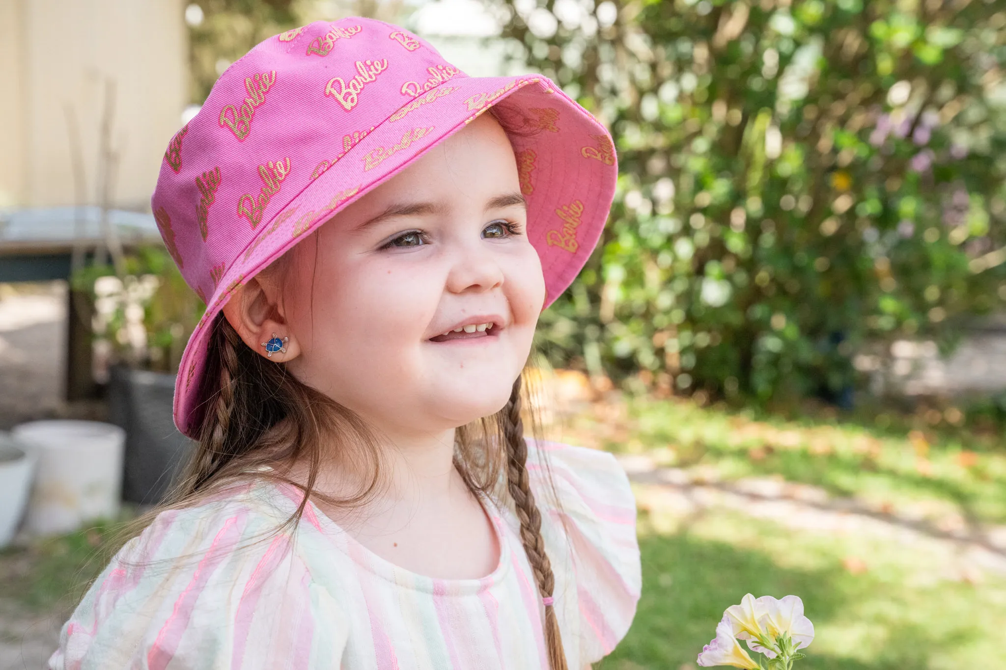 A smiling young girl in a pink sun hat looking up in the garden