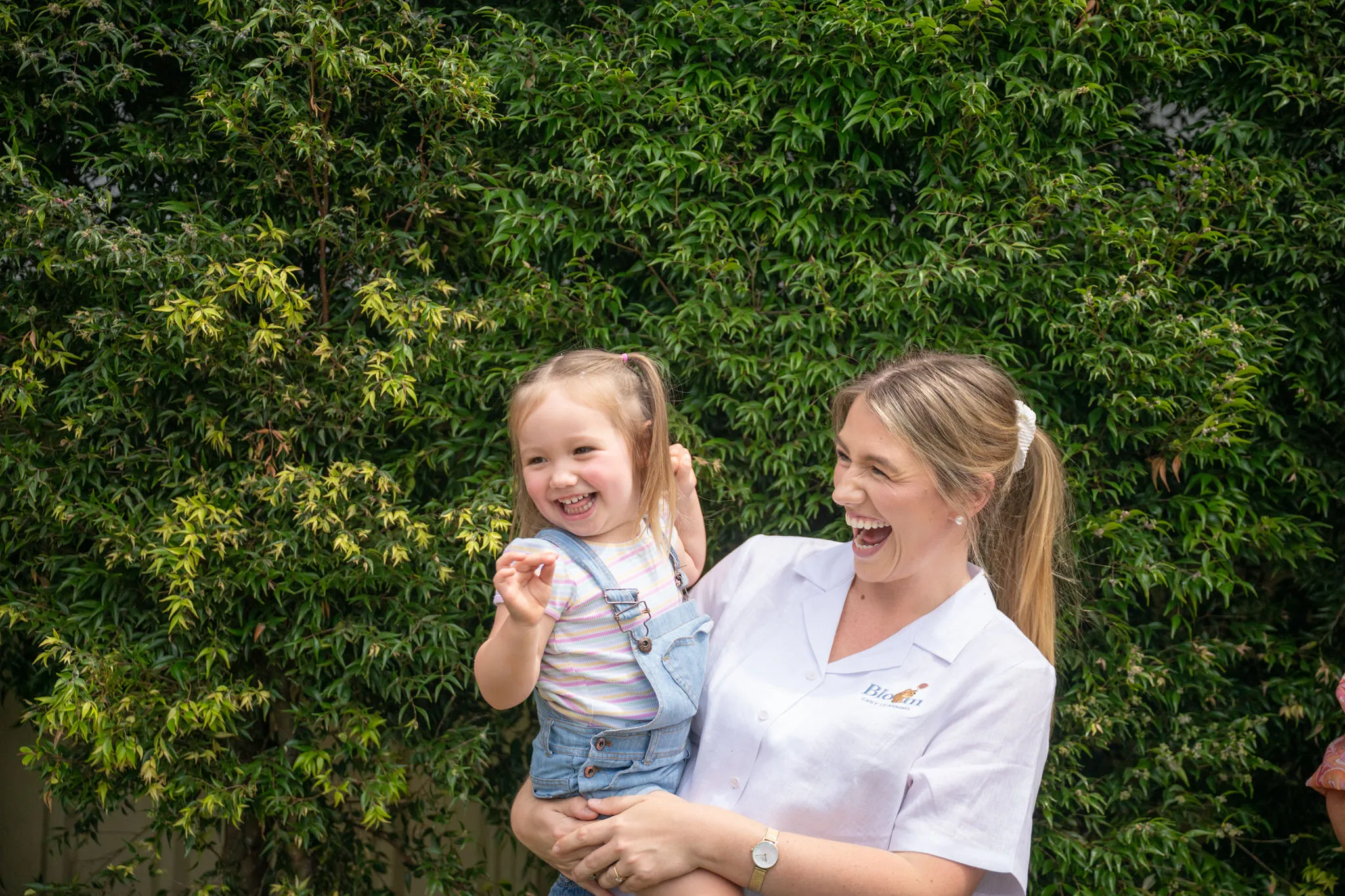 A smiling Bloom educator holding a laughing toddler in the garden