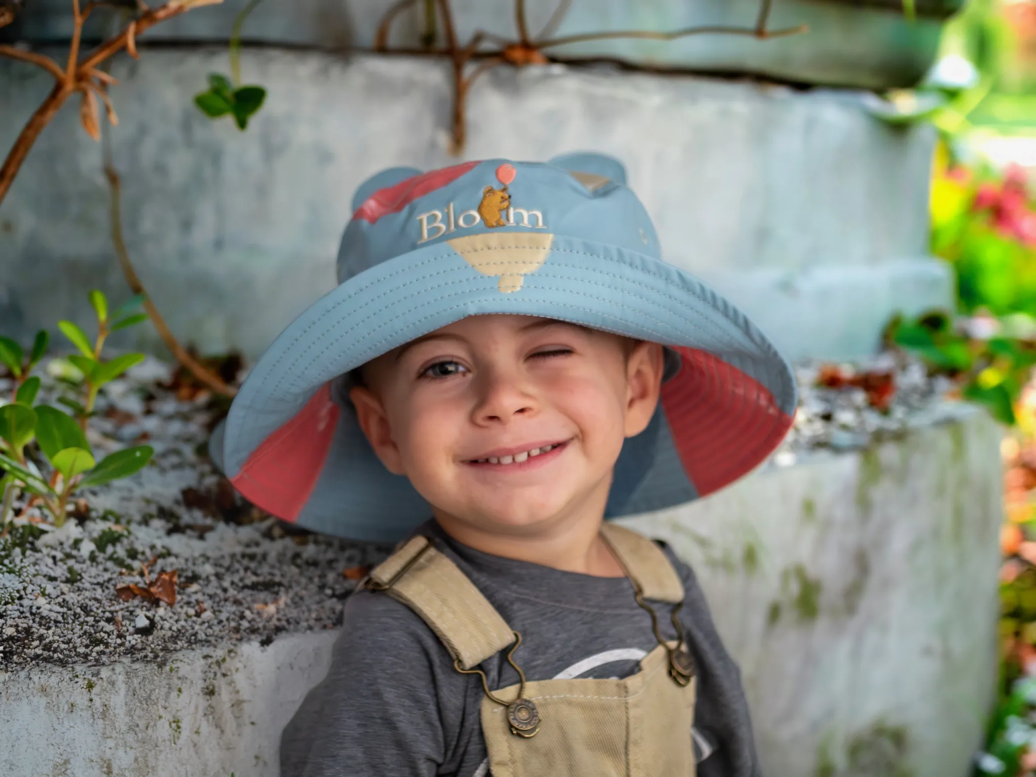 A smiling boy in a Bloom bucket hat in the garden